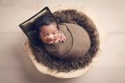 wavy newborn baby faux fur in brown with baby swaddled in brown wrap and dark green pillow in wood bowl