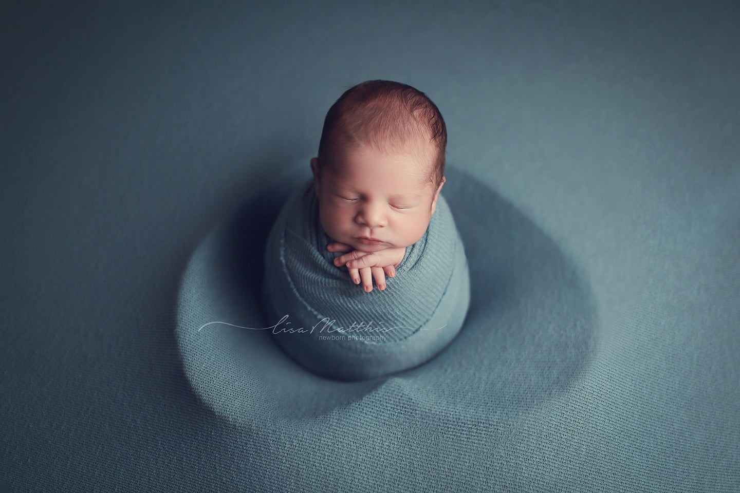 newborn baby boy in blue swaddle wrap and posing fabric with heart bowl