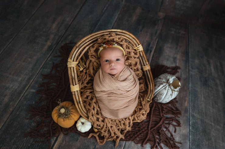 newborn baby girl sitting in bamboo chair with macrame rug, swaddled and headband