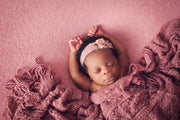 black newborn baby girl with pink posing fabric, ruffle blanket and flower headband with arms above head