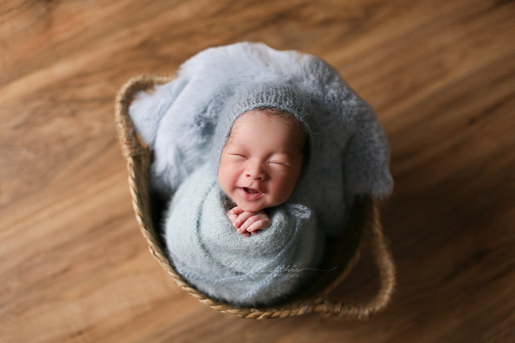 newborn boy in basket with light blue faux fur rabbit skin and furry, swaddling wrap with hat by custom photo props