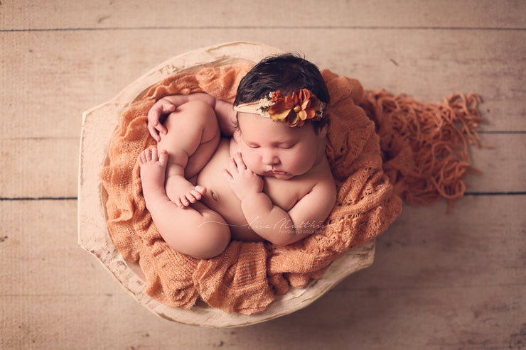 newborn baby girl with orange ruffle layering fabric and orange headband