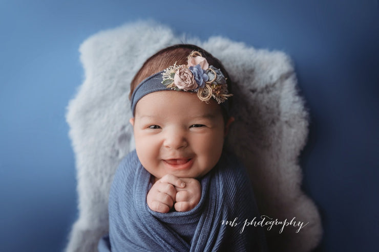 newborn girl in blue swaddle wrap, gray fur and blue and pink flower headband photography props