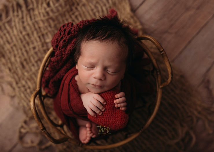 newborn baby boy or girl with red layered doily and swaddling wrap, holding red heart by custom photo props