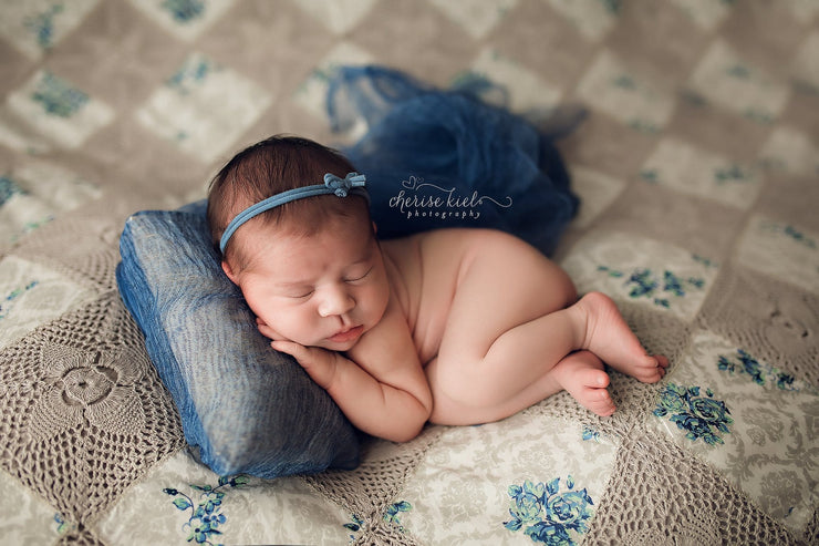 newborn girl with blue headband, and pillow on quilt photography props