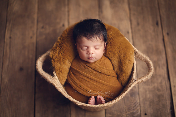 newborn baby in copper colored rabbit pelt and swaddling wrap
