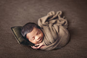 light brown fuzzy newborn baby swaddled in wrap and with small pillow