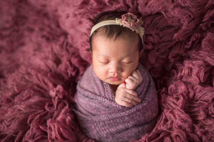 newborn baby girl swaddled in potato sack pose with fuzzy purple stretch swaddling blanket wrap