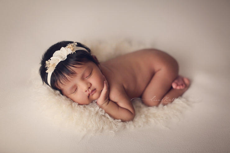 newborn girl posing on belly with ivory headband and  faux flokati fur