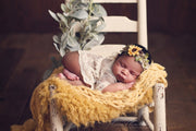 newborn girl on chair with yellow faux flokati fur and chunky blanket and sunflower headband photography prop