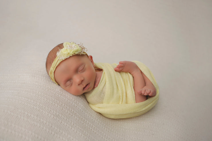baby girl swaddled in yellow wrap and yellow flower headband for baby's first photos
