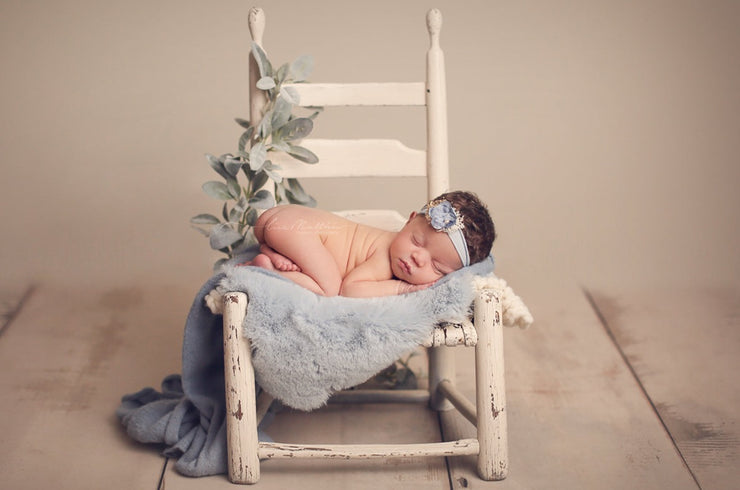 newborn baby girl with blue flower headband on chair and green foliage