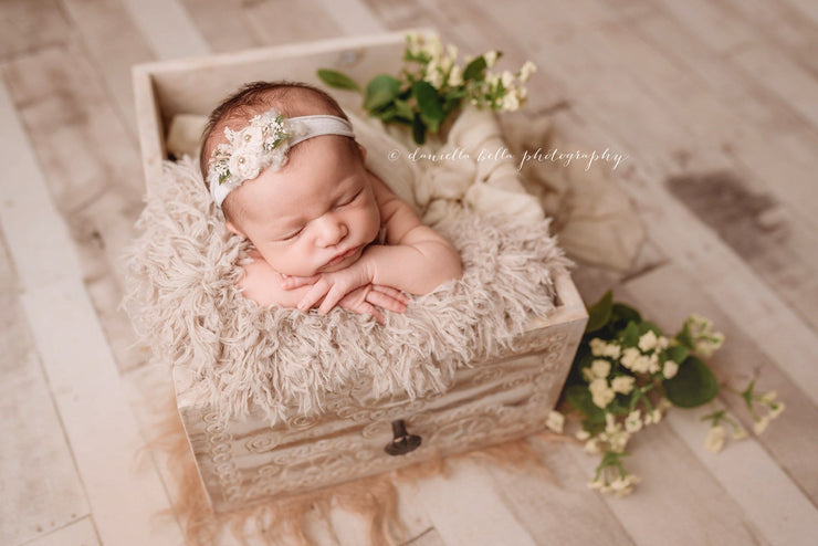 newborn baby girl in white craved drawer with fur and headband photo props